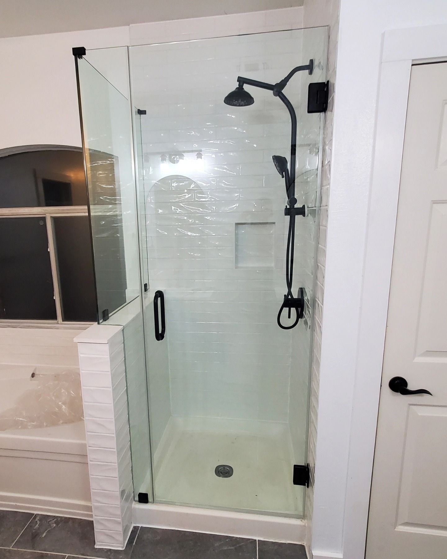 A modern glass shower with black fixtures. It has a rain shower head, handheld shower, and a small inset shelf.