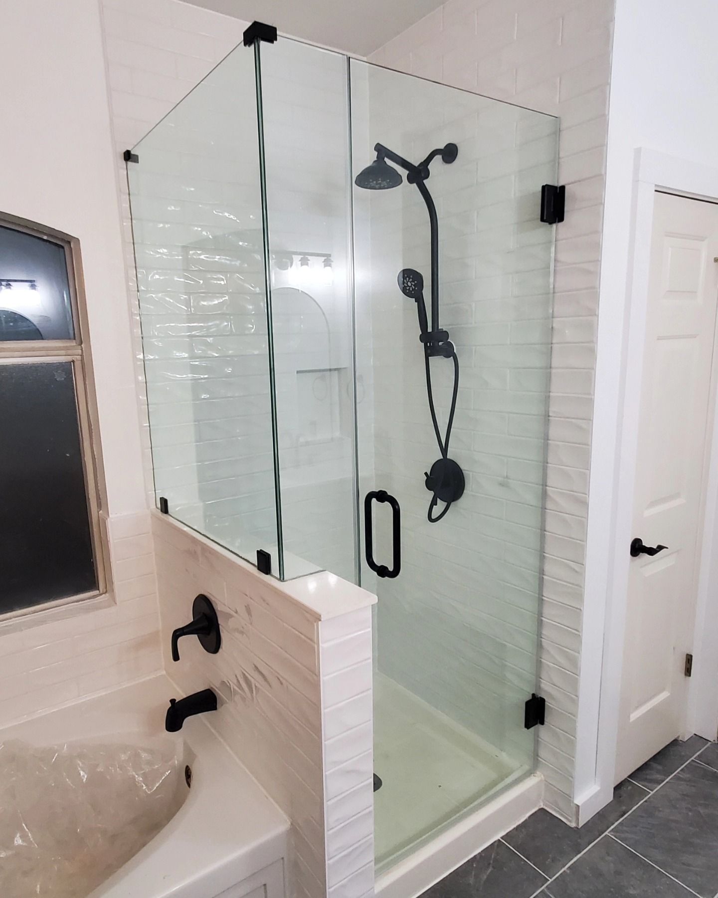 A modern bathroom with a glass shower enclosure, black fixtures, and a bathtub.