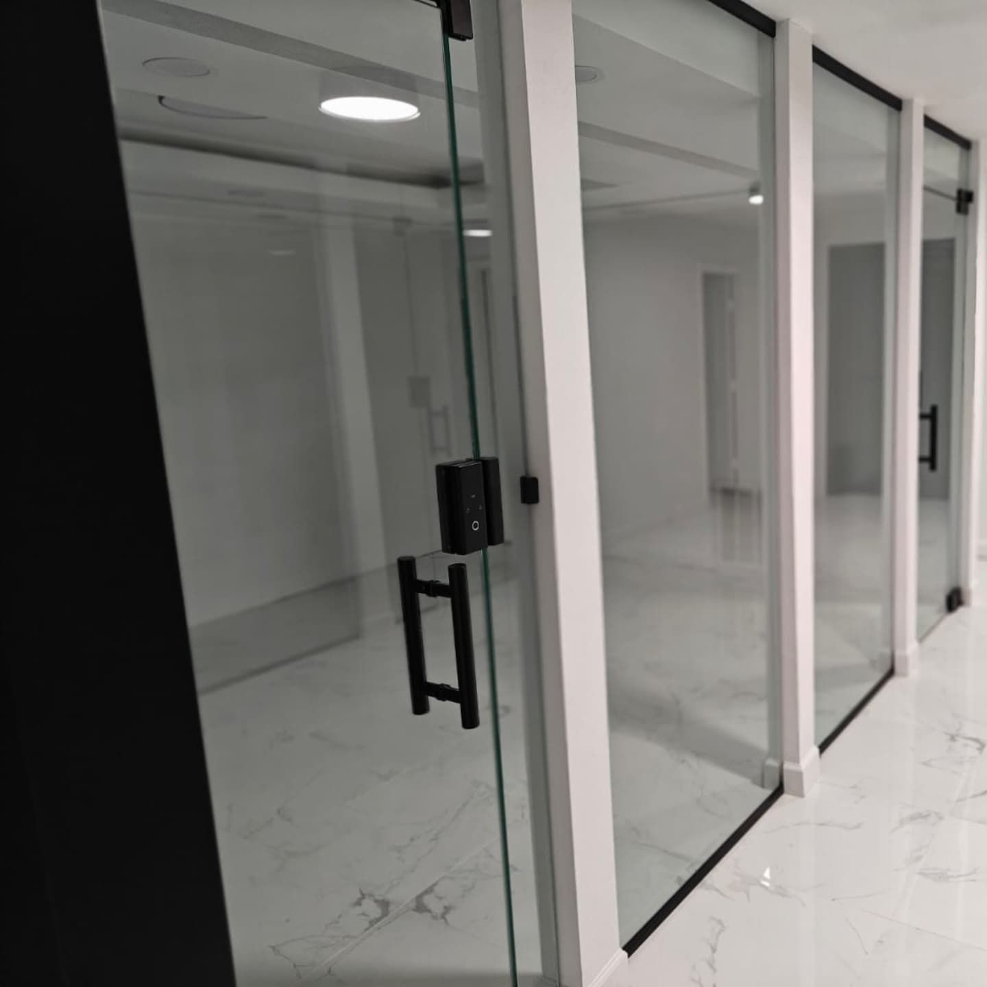 A row of glass-walled rooms with black door handles, white frames, and a marble floor.