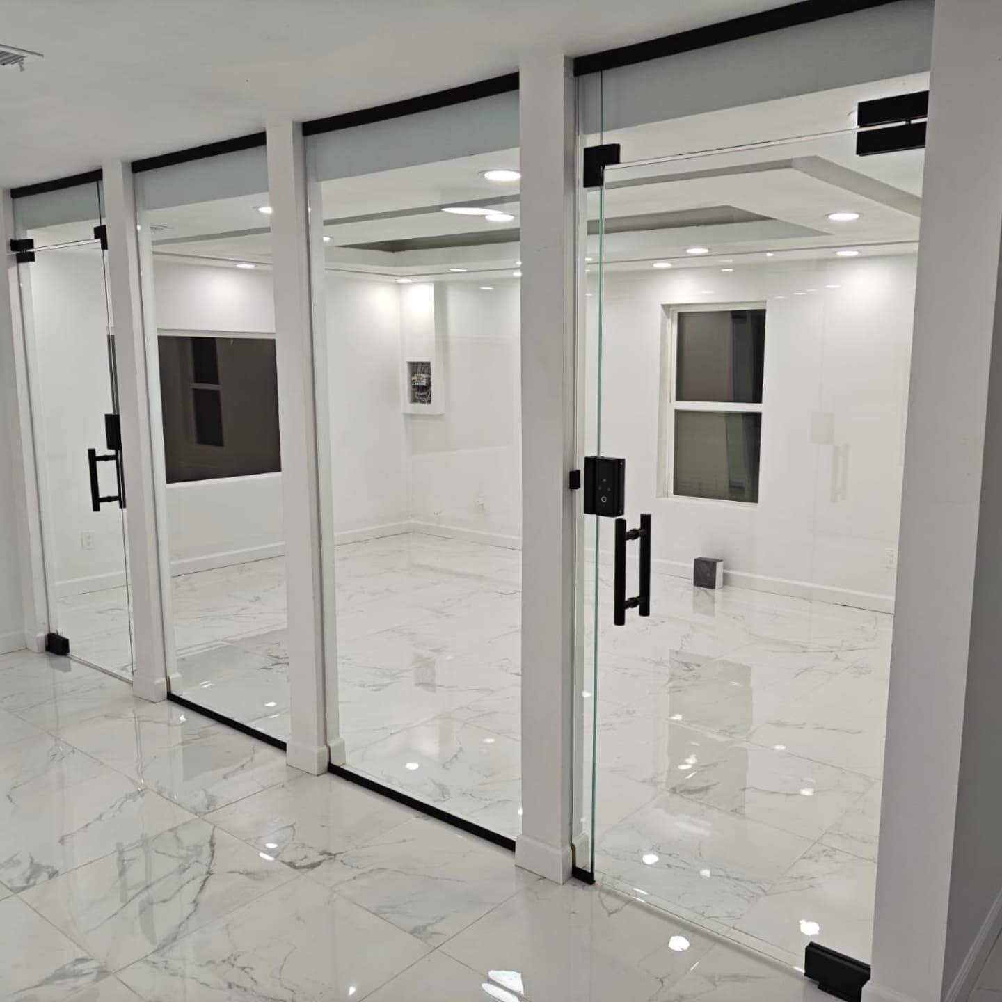 Three glass-walled rooms with black door handles in a modern, white-walled interior. Marble flooring.