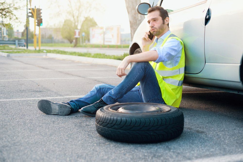 Man Sitting Beside a Car With a Wheel Removed — Batteries & Tyres in Wellington, NSW
