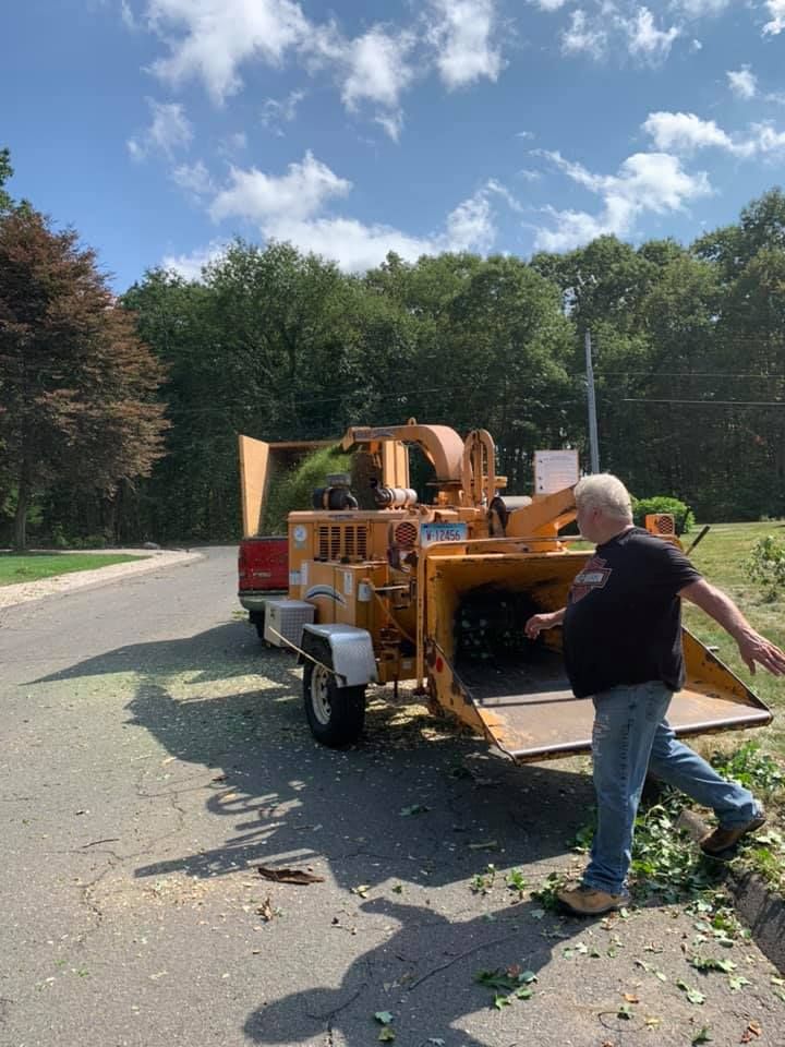 A man is standing next to a tree chipper on the side of the road.