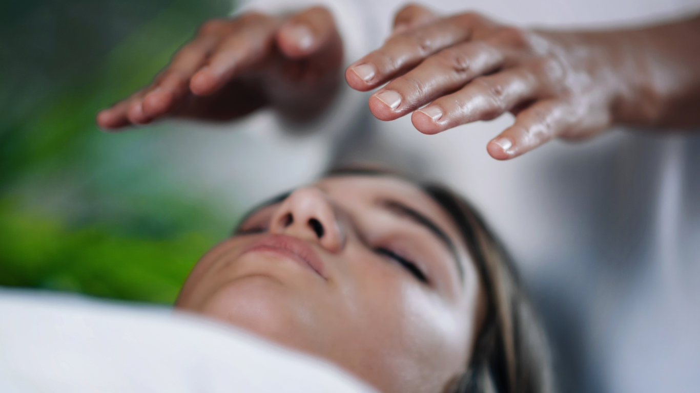 A woman is getting a healing session with her hands on her head.