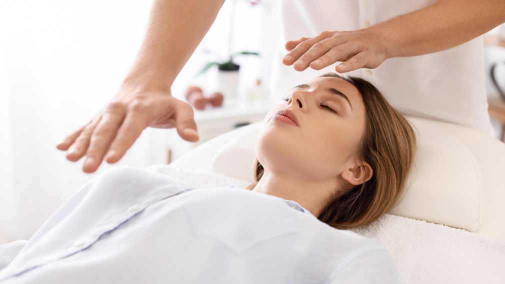 A woman is laying on a bed getting a reiki treatment.