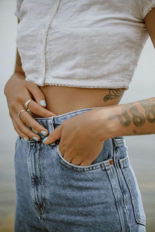 A woman with a tattoo on her stomach is putting her hand in her pocket.