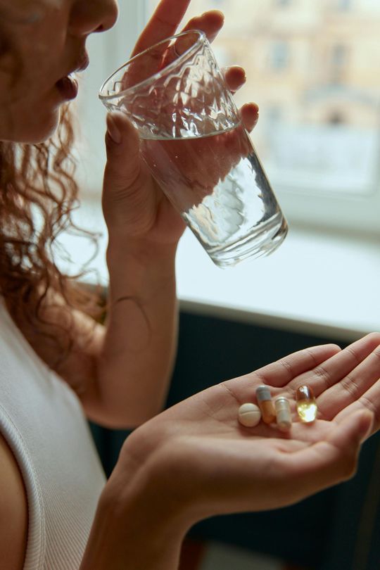A woman is taking a pill while drinking a glass of water.