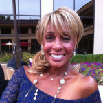 A woman wearing a blue top and a necklace is smiling for the camera.