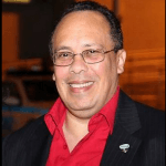 A man wearing glasses and a red shirt is smiling for the camera.