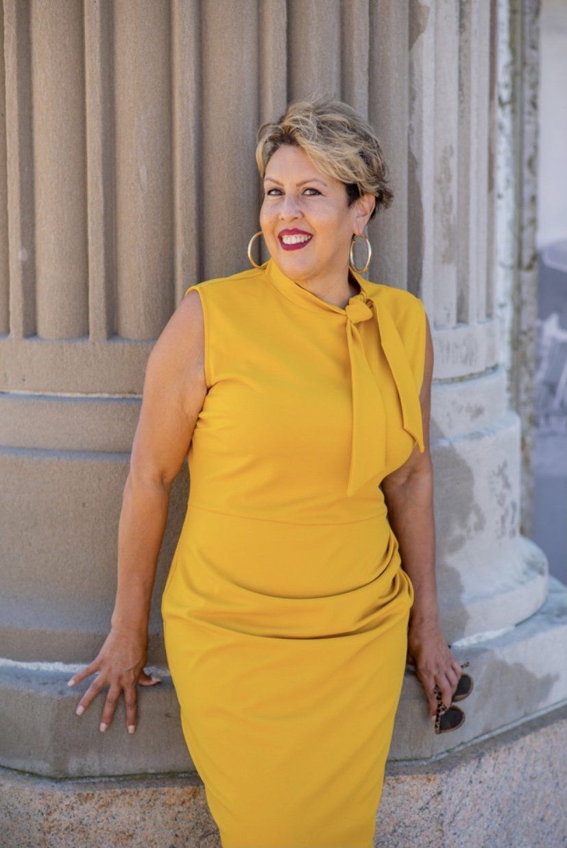 A woman in a yellow dress is leaning against a pillar.