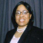 A woman wearing glasses and a pearl necklace is smiling for the camera.