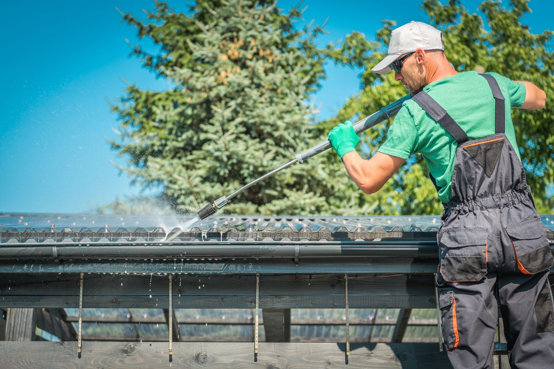 Worker in green shirt cleaning a rooftop gutter with a pressure washer under a blue sky Worker in green shirt cleaning a rooftop gutter with a pressure washer under a blue sky