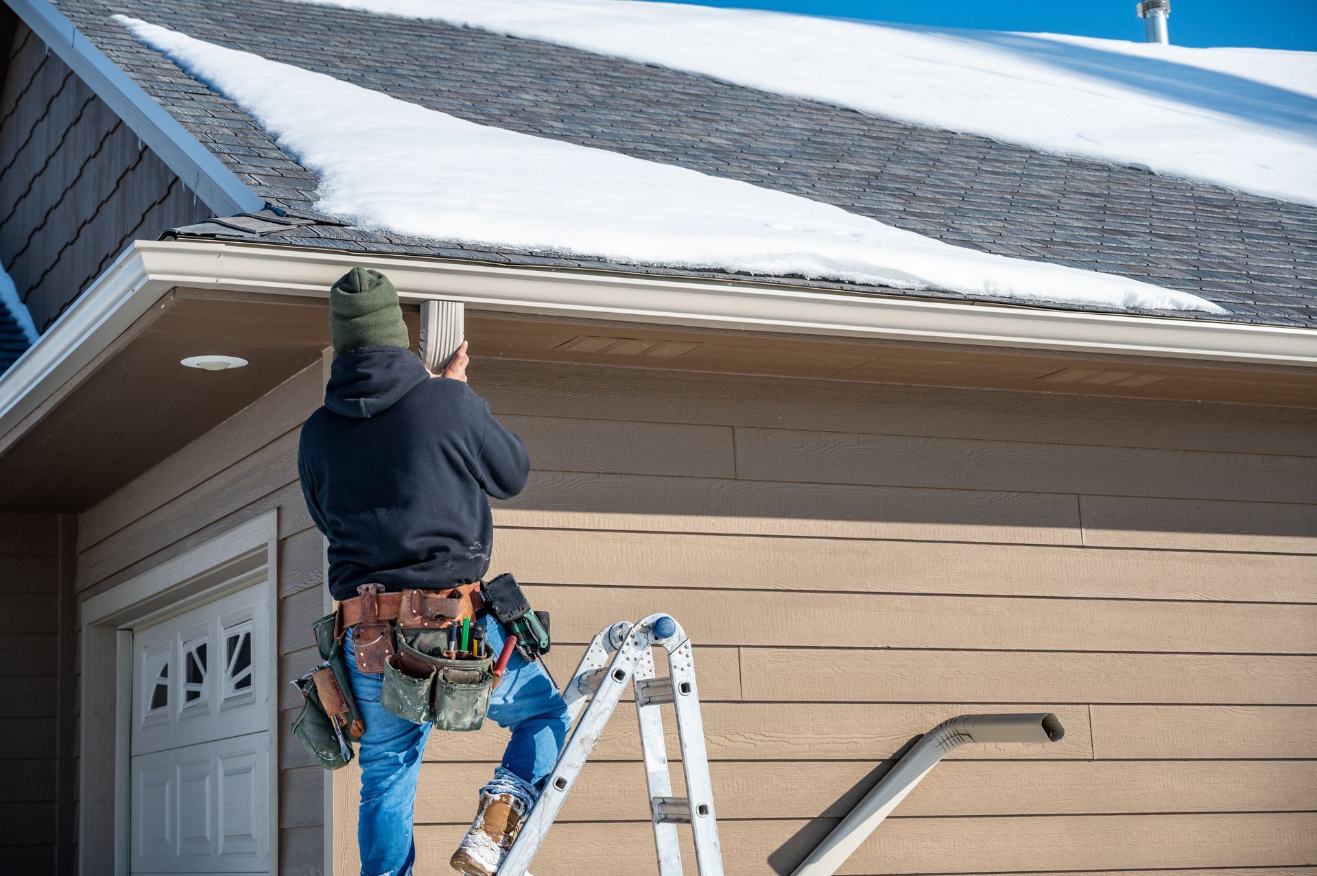 Worker on a ladder repairing a house roof and eaves in winter snow Worker on a ladder repairing a house roof and eaves in winter snow