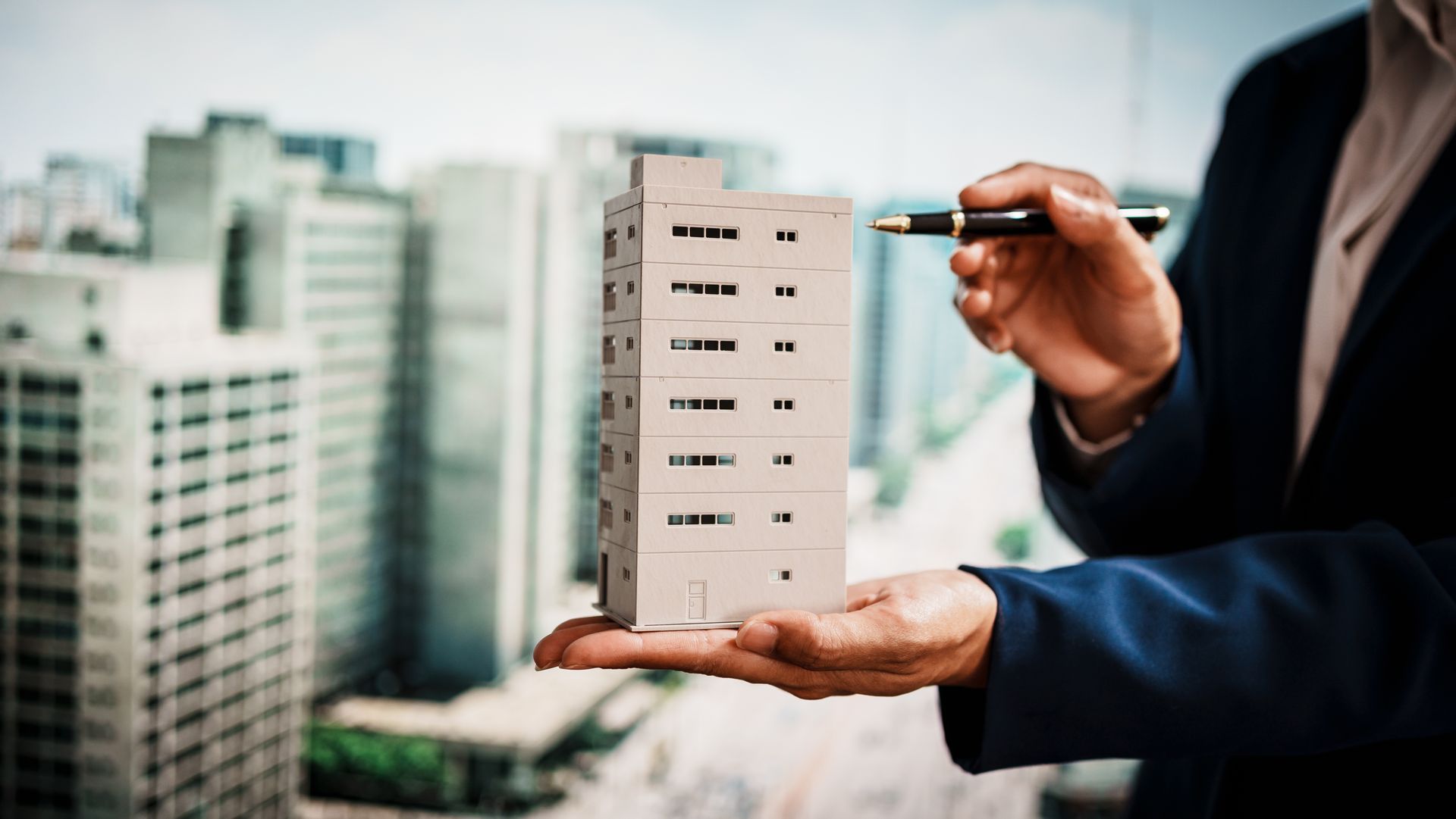 Hand holding a miniature apartment building model, examined with a pen.