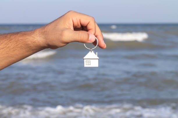 Hand holding a house-shaped keychain in front of a blue ocean.