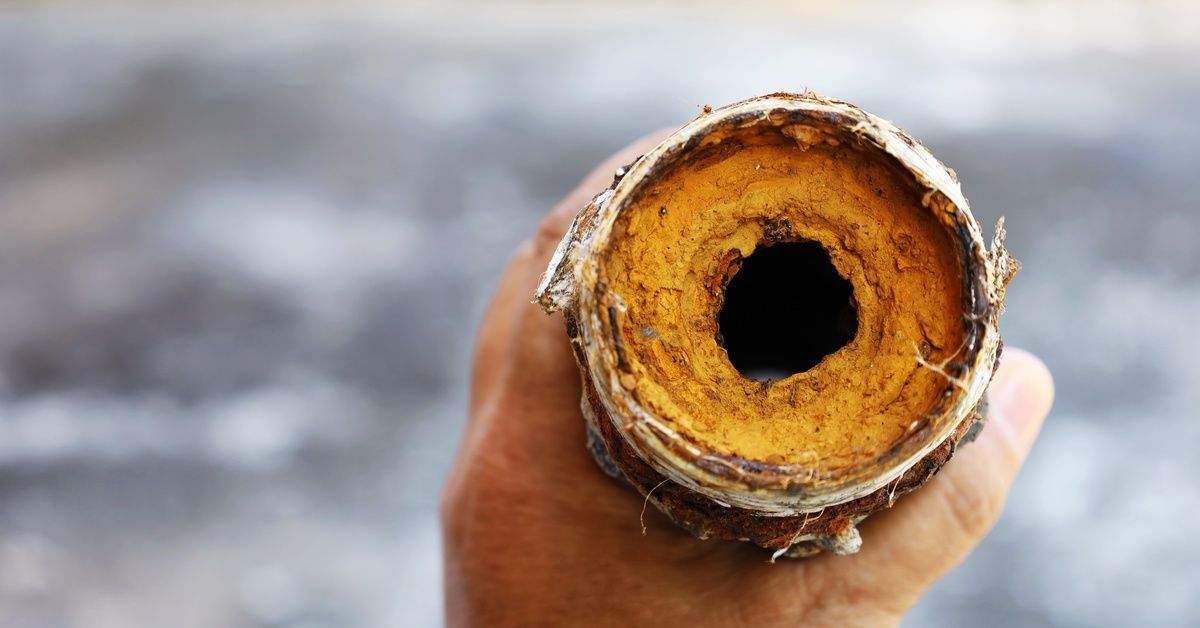 A hand holding an older pipe that's very clogged. There is a small hole in the backed up material.