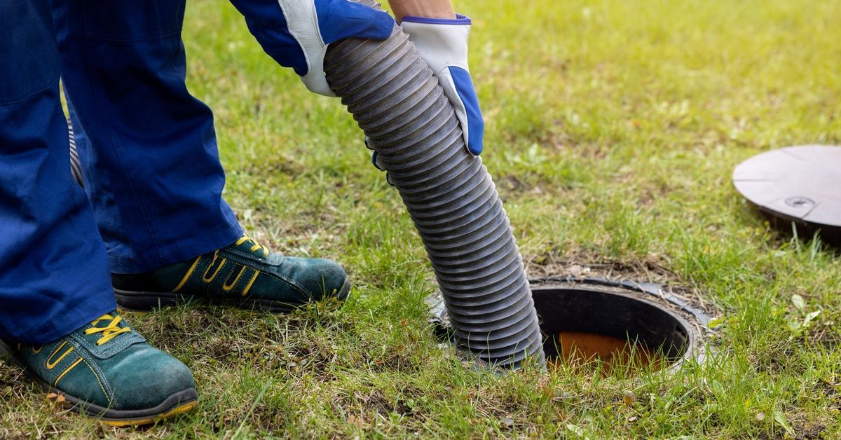 Someone holding a large tube that's leading into a home's sewer drainage system. The lid is sitting off to the side.
