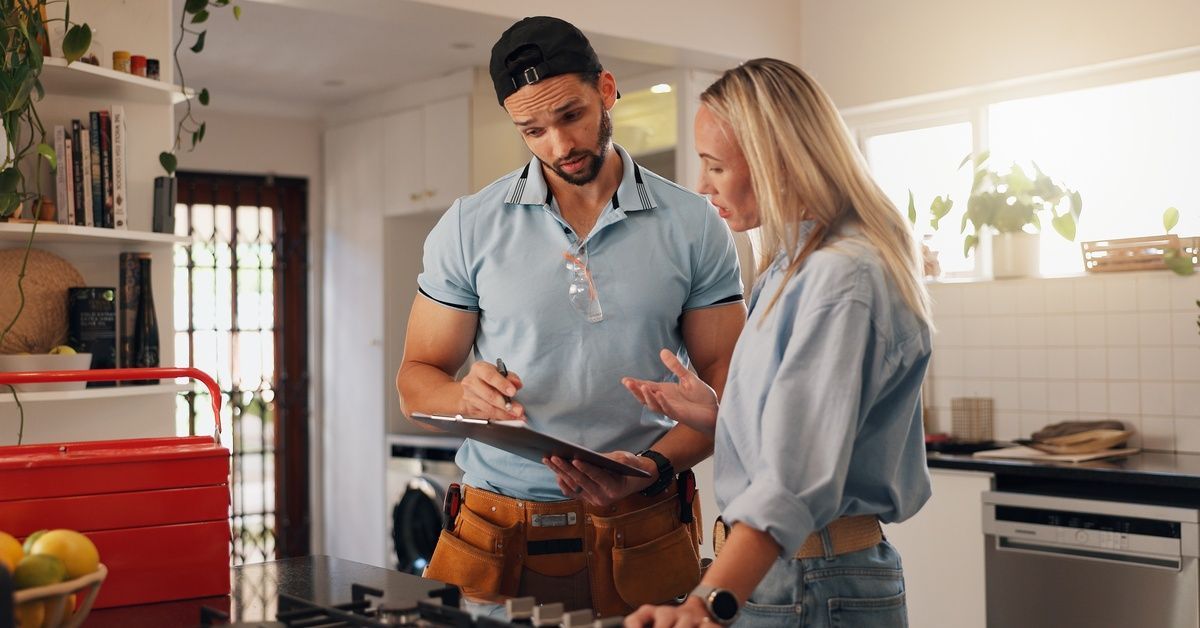 A plumber showing a woman a clipboard that he is holding. She is holding one hand out and looks a little confused.
