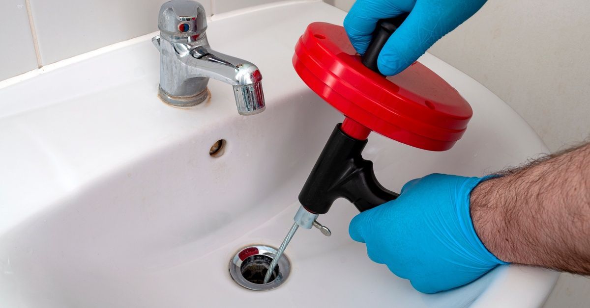 Someone using a plumber's snake to clean out a clogged sink drain. He's spinning the top of the mechanism to clean it out.
