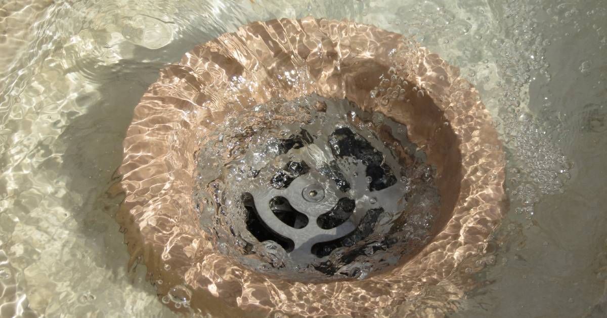 A swirling pattern of clear water drains into a peach-colored sink with a stainless steel drain cover.