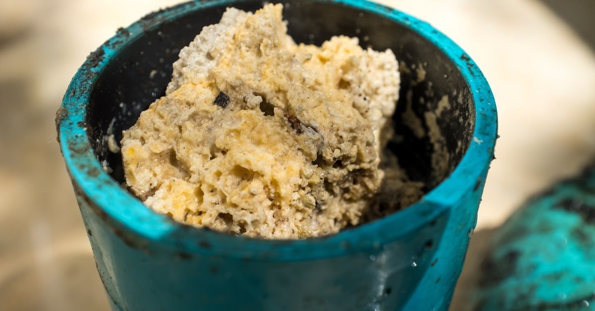 A cross-section of a teal-colored pipe with a buildup clump of thick fat, oil, and grease stuck in it.
