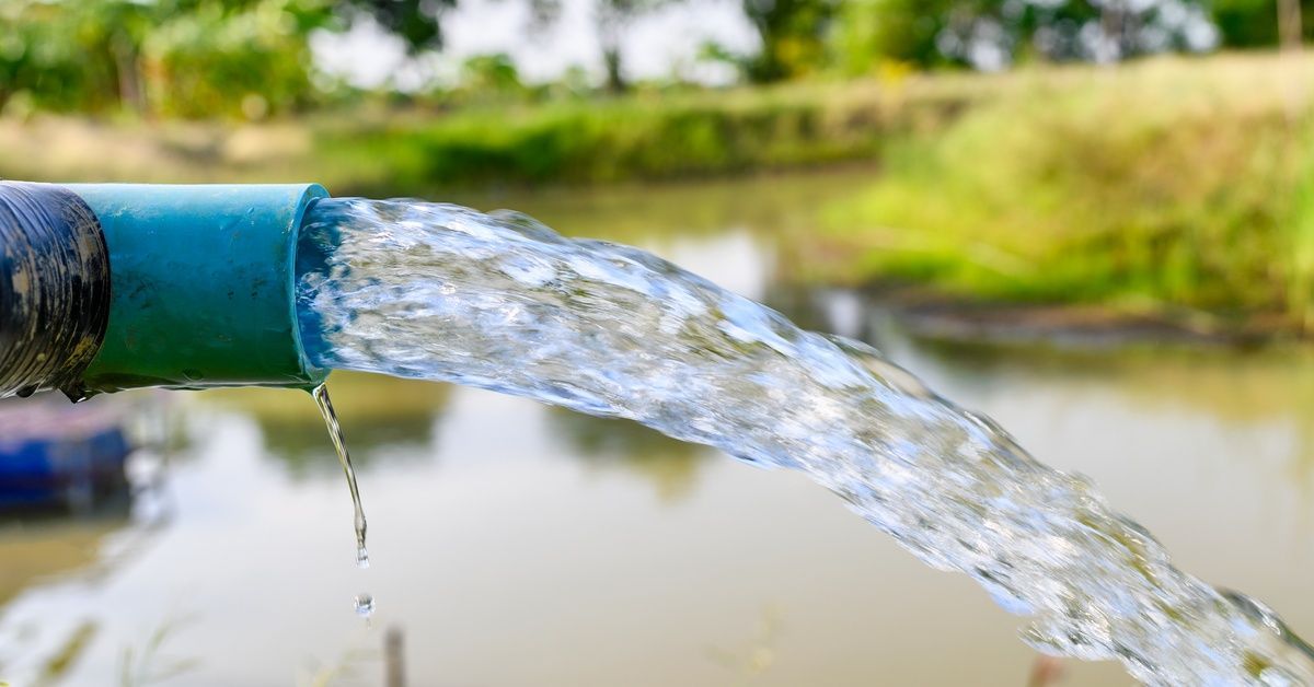 A drain pipe leading to an outdoor water source with clear, clean water flowing out of it at a high speed.