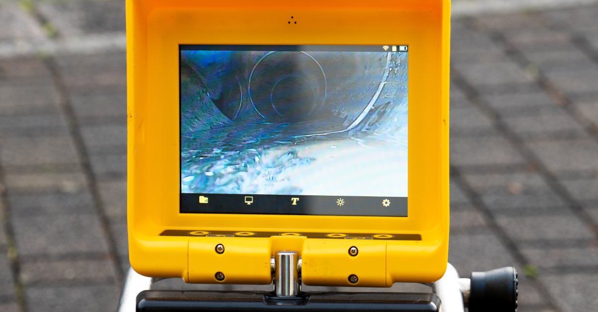 A screen held outside shows the inside of a drain system. The stone walkway behind the screen is blurry.