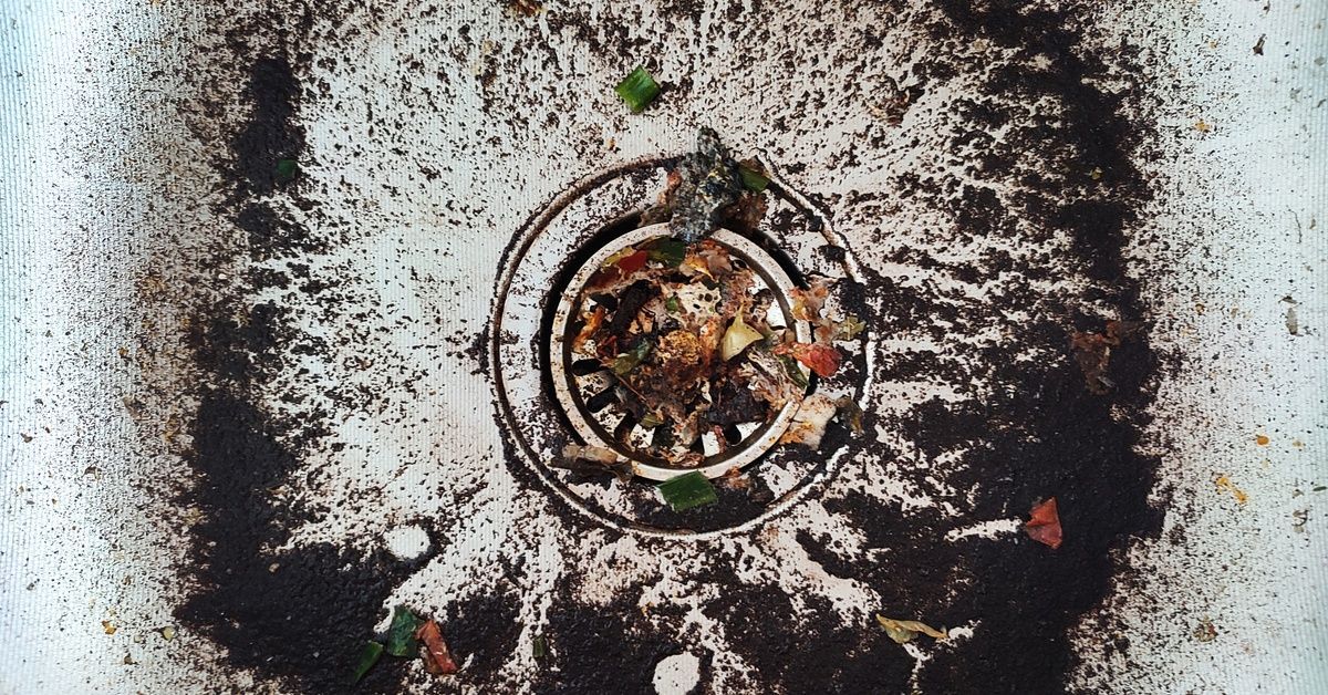 A top-down view of a white sink covered with coffee grounds, vegetable peels, and other food debris.