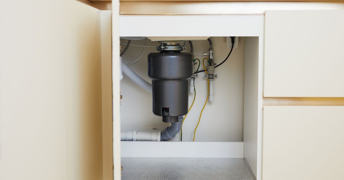 A newly built kitchen with white under-the-sink cabinets. One is open, showing a black garbage dispo