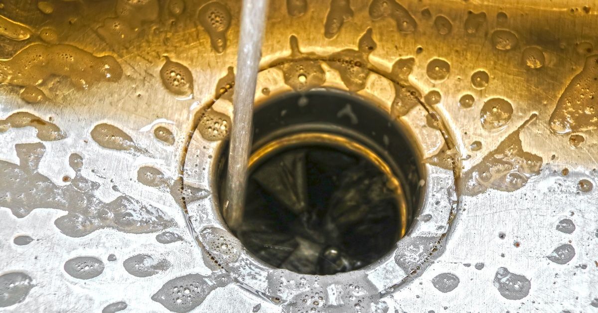 A stream of water flowing from a faucet into a garbage disposal in a silver sink surrounded by bubbles.