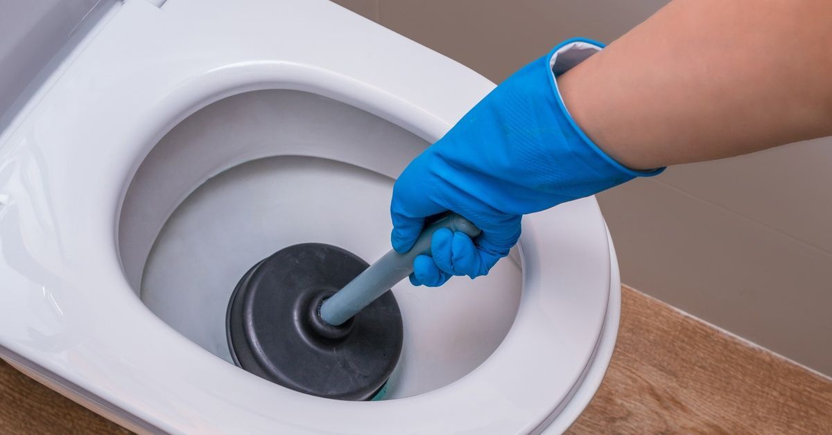 A hand wearing a long, blue glove uses a plunger with a gray handle on a white toilet.