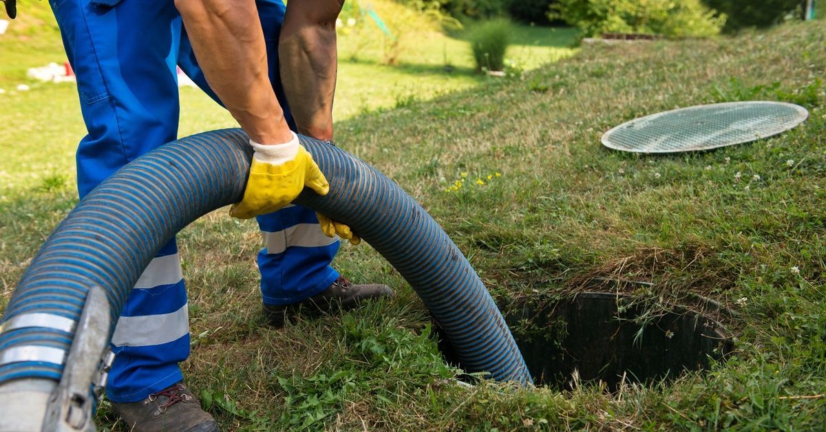 A person wearing blue pants with reflective tape around the ankles empties a septic tank into a deep