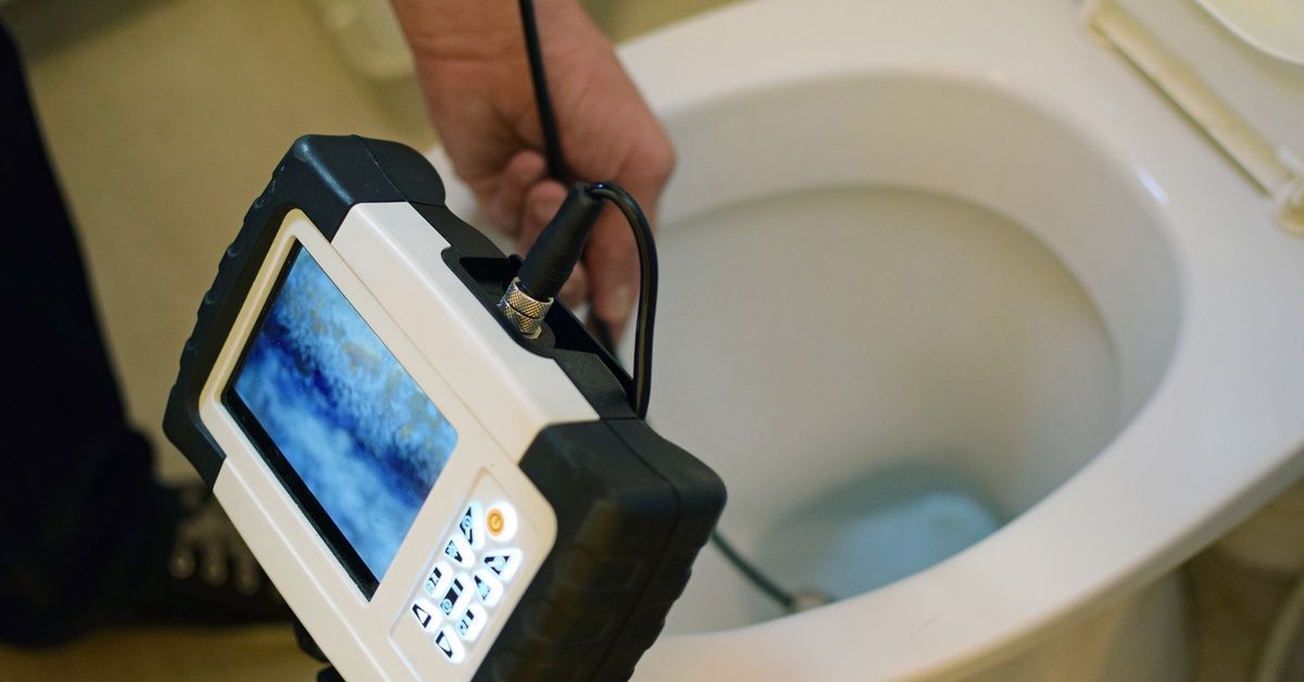 A close-up of a drain camera inspection screen as a contractor feeds a wire into a toilet bowl.