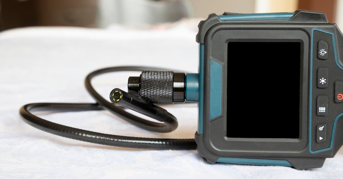 A close-up of a drain inspection camera lying on its side on a towel with a blank, black screen.