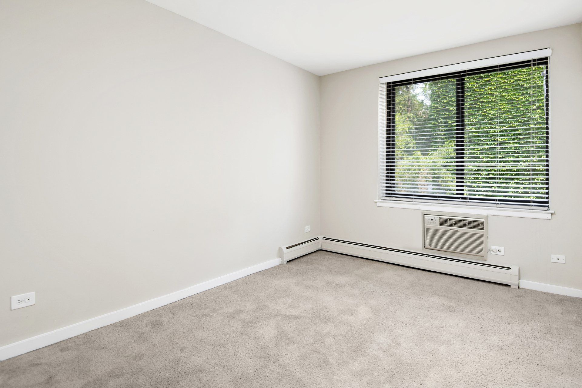 An empty bedroom with a window and air conditioner at Reside on Pine Grove.