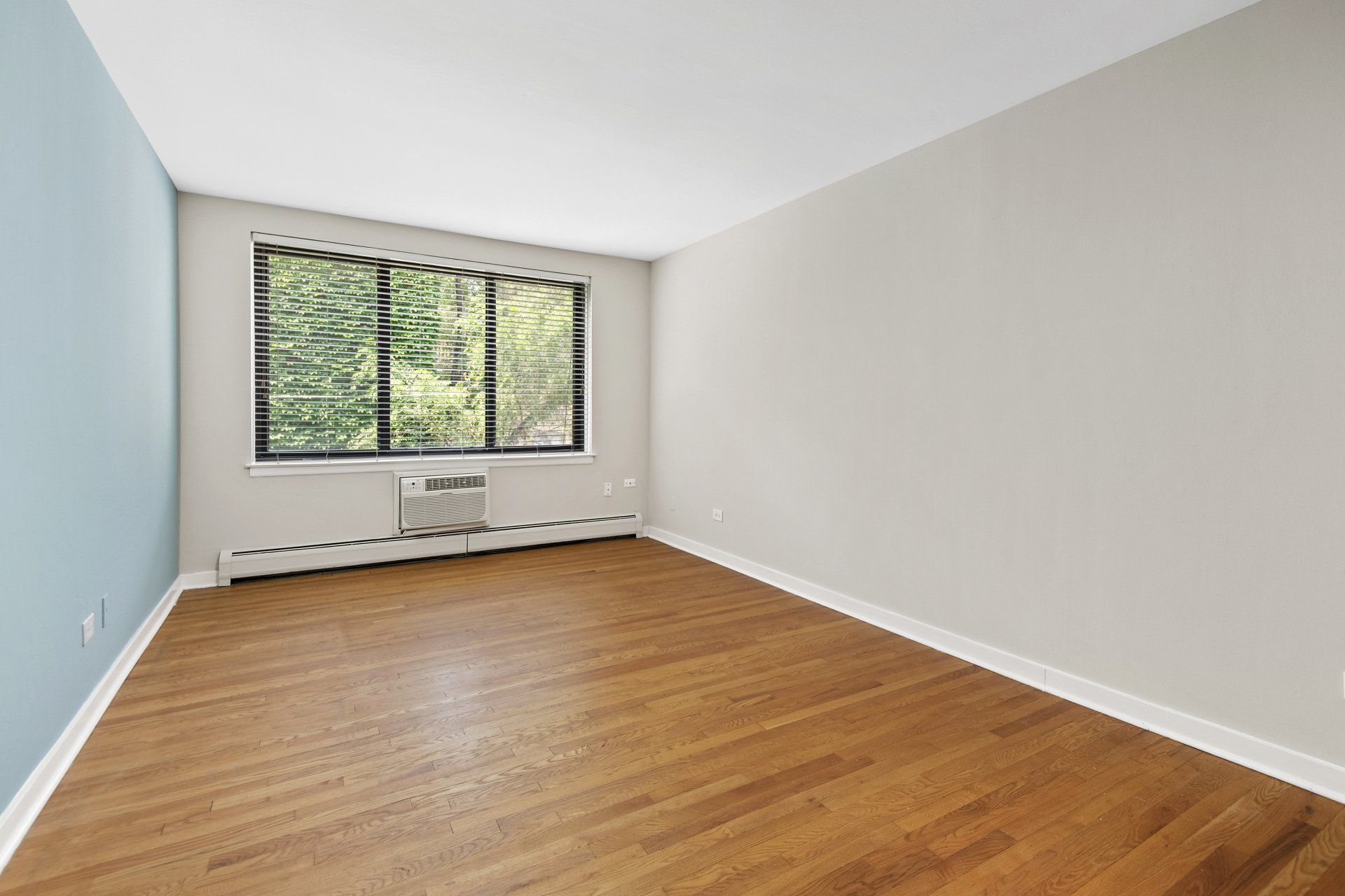 An empty living room with hardwood floors and a large window at Reside on Pine Grove.