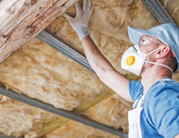 A man wearing a mask is insulating the ceiling of a house.