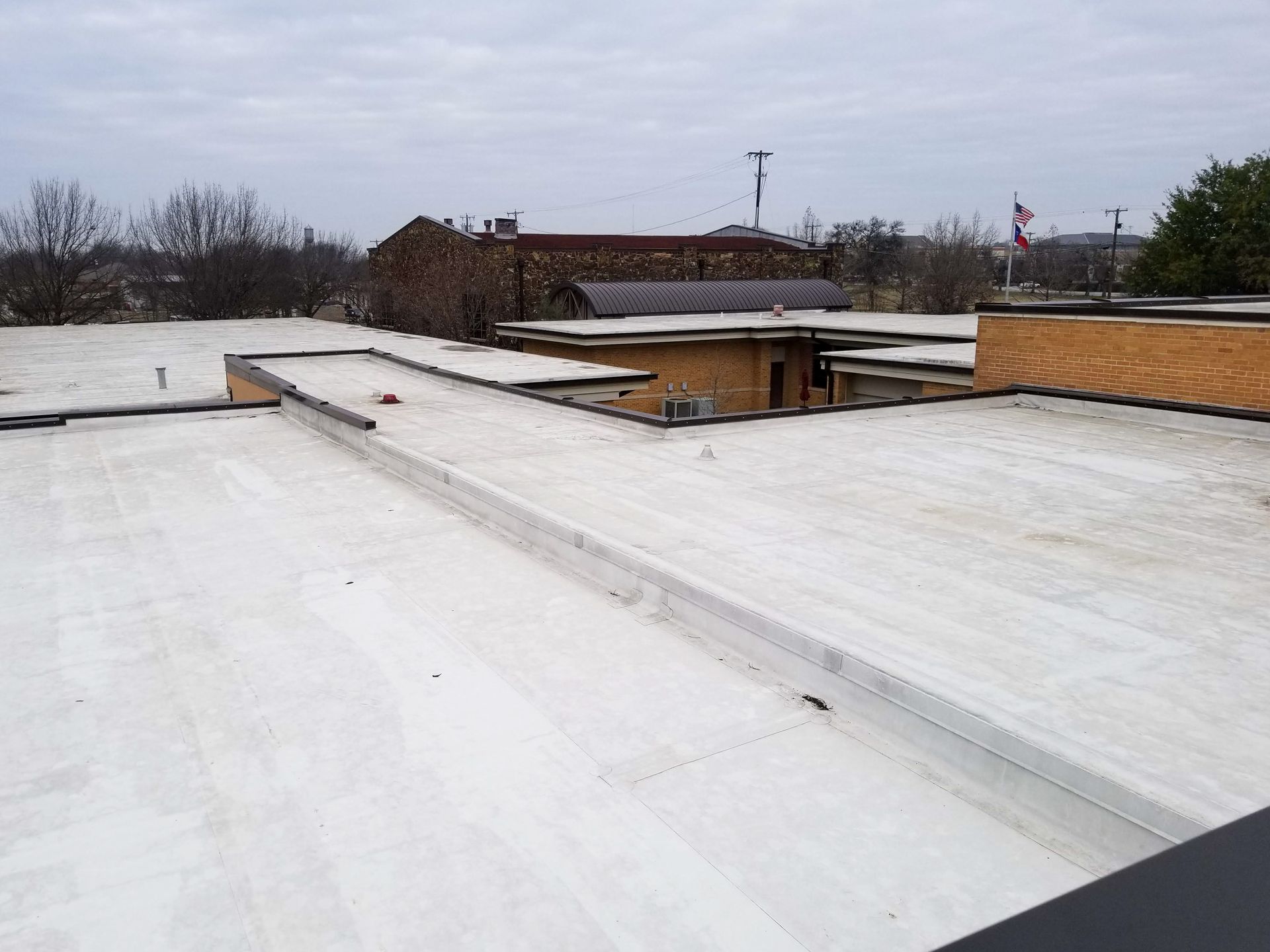 The roof of a building with a white roof and trees in the background.