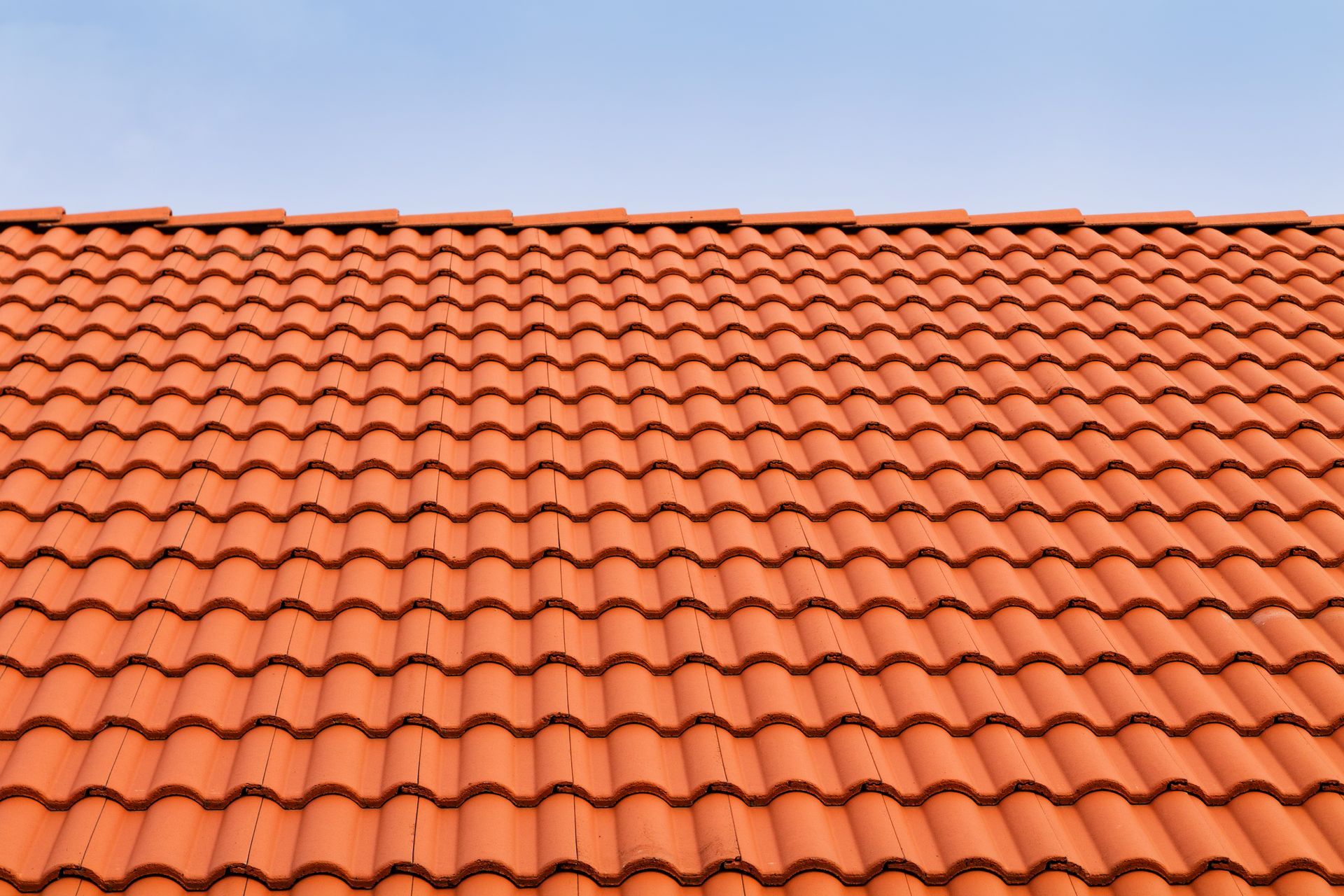 A close up of a red tiled roof with a blue sky in the background.