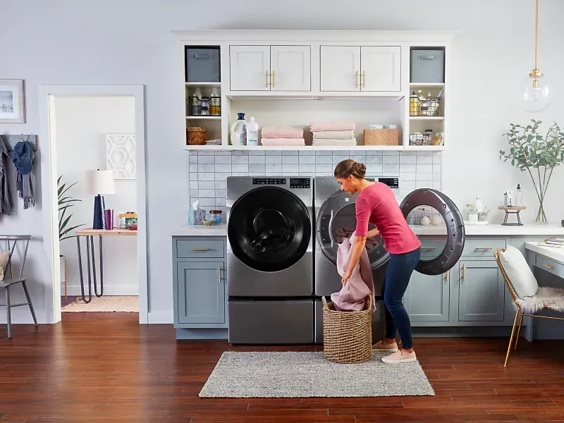 A woman is putting clothes in a washer and dryer in a laundry room.