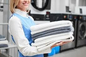 A woman is holding a pile of towels in a laundromat.