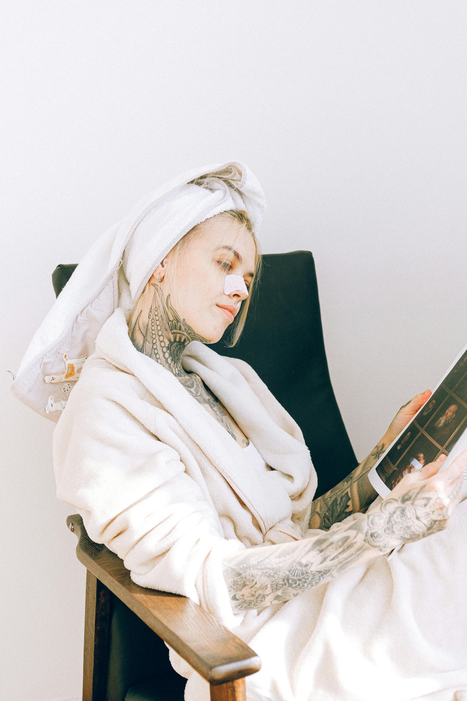 A woman with a towel wrapped around her head is sitting in a chair reading a book.