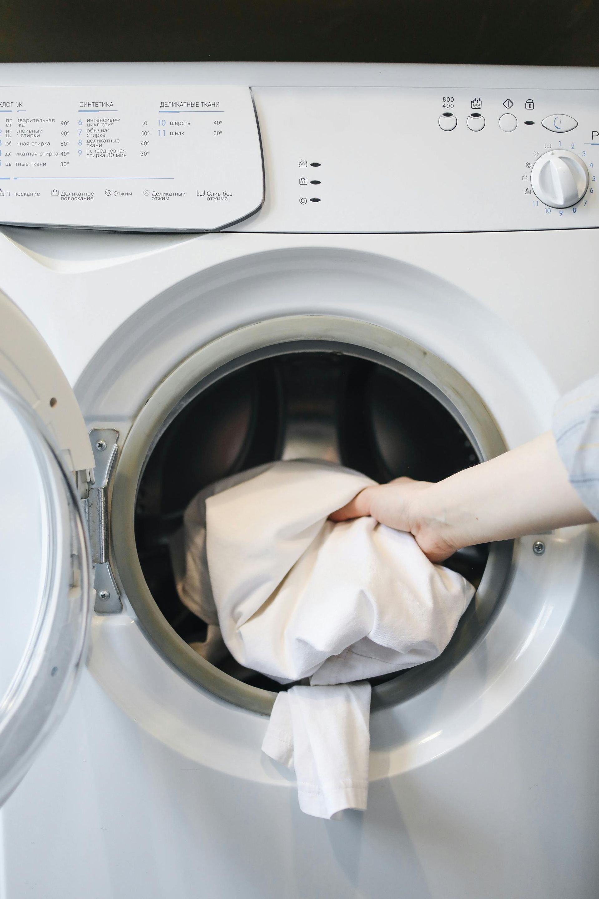 A person is putting a white shirt in a washing machine.
