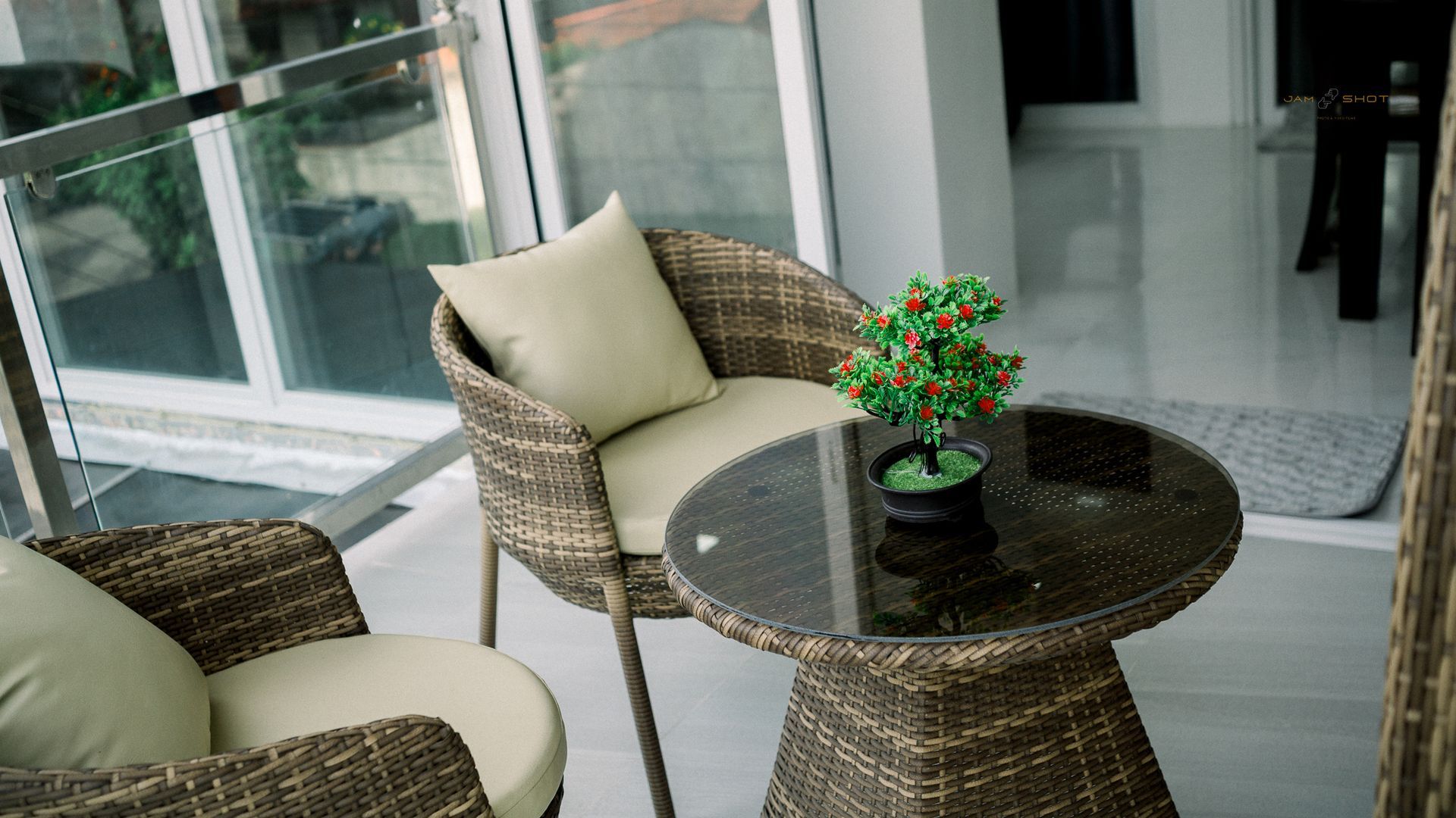 Two wicker patio chairs with beige cushions and a small round glass-top table with a mini potted plant on a balcony.