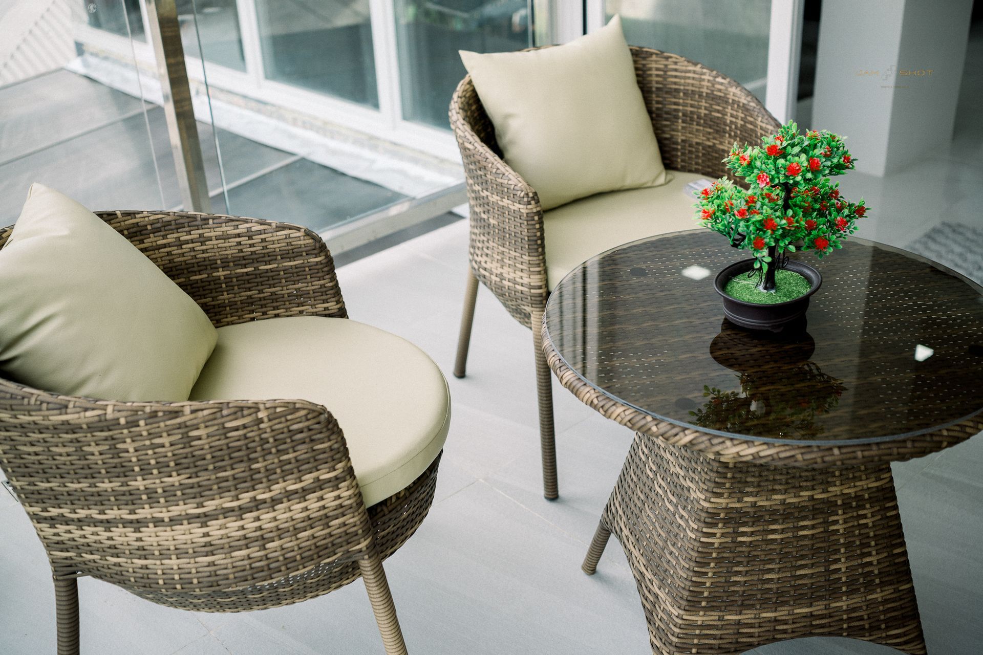 Two wicker chairs with beige cushions and a small round table with a potted plant on a patio.