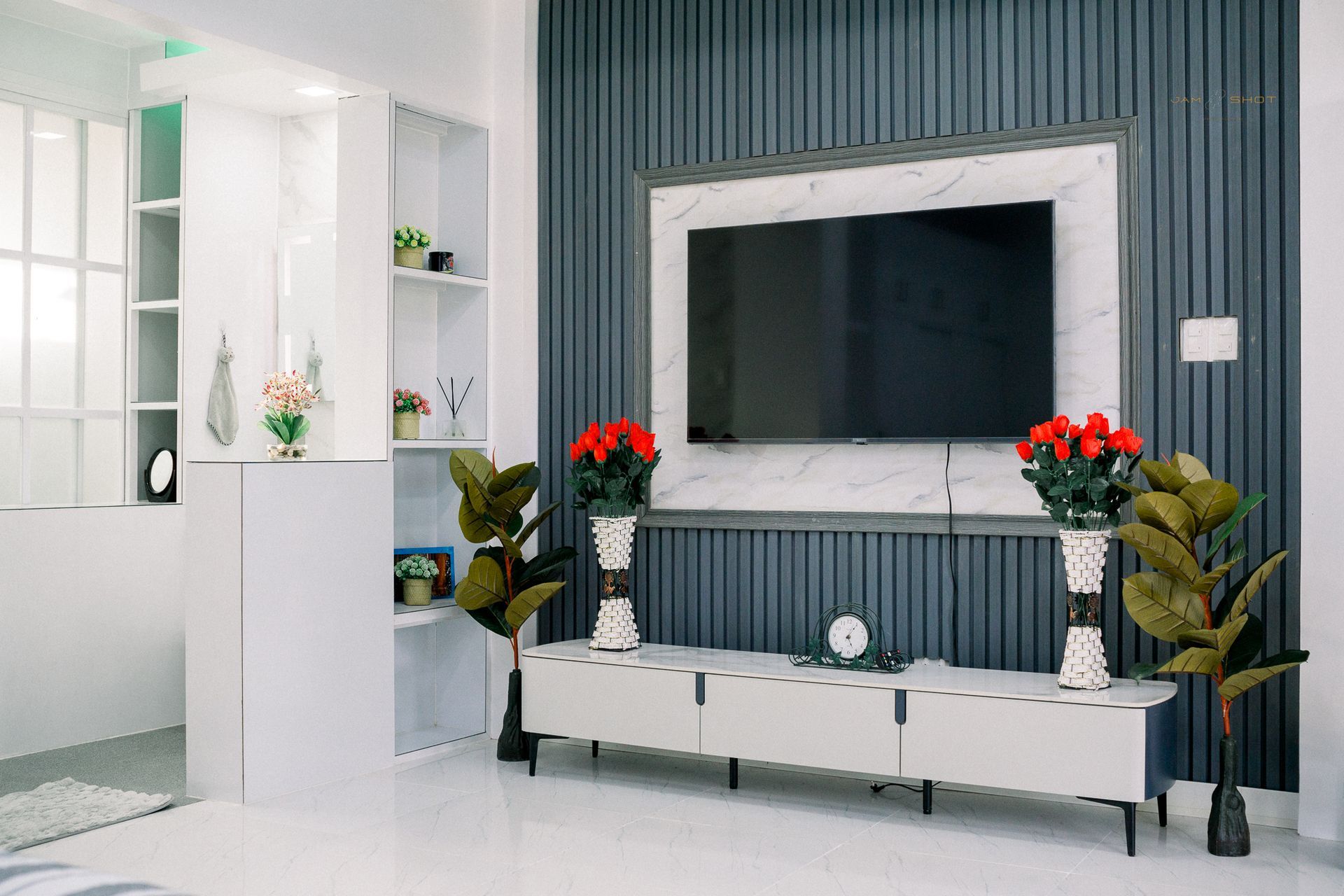 A television mounted on a marble-patterned panel against a dark blue slatted wall, with a white media console below.
