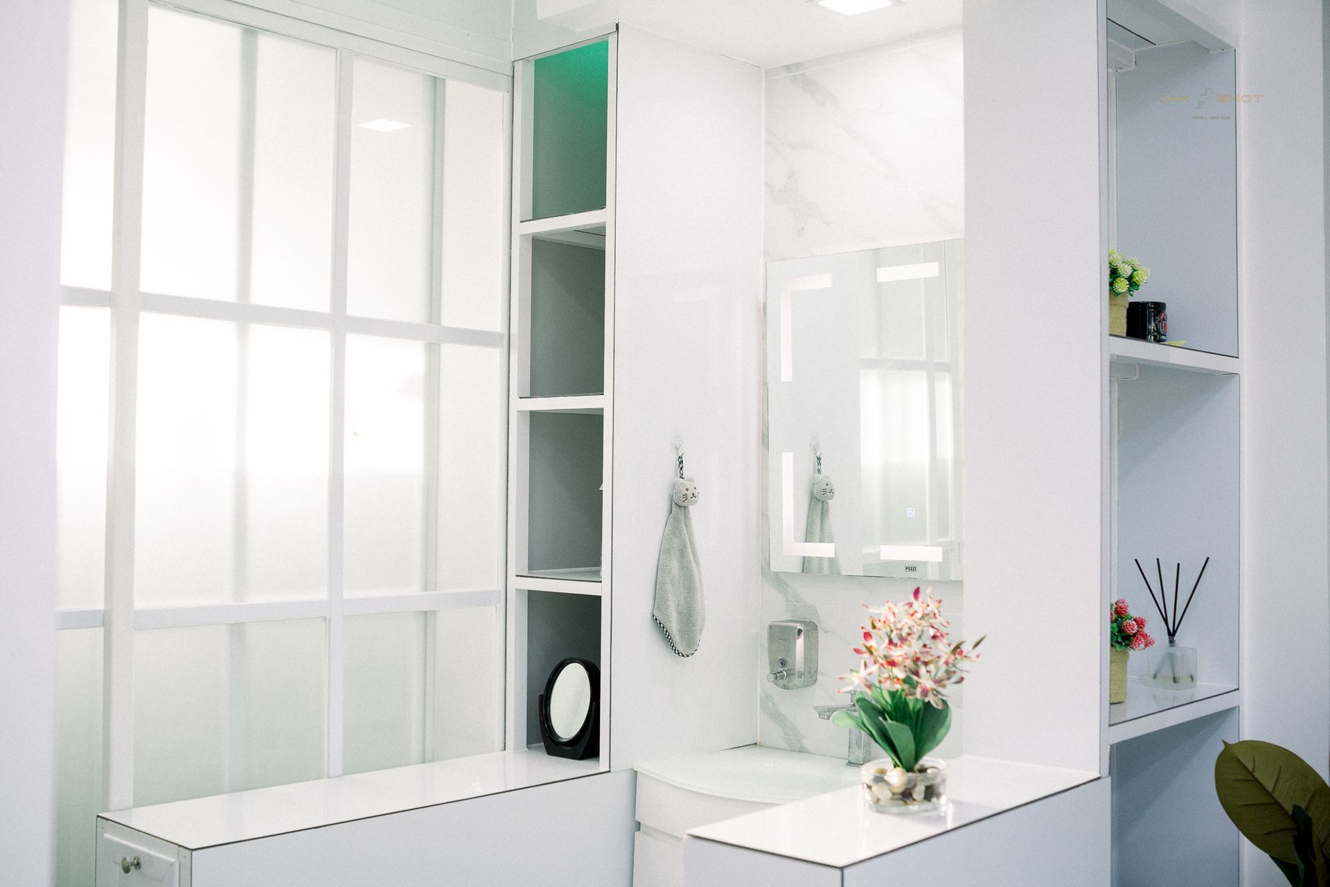 A modern, minimalist bathroom with white walls, shelves, a basin, and a translucent window panel.