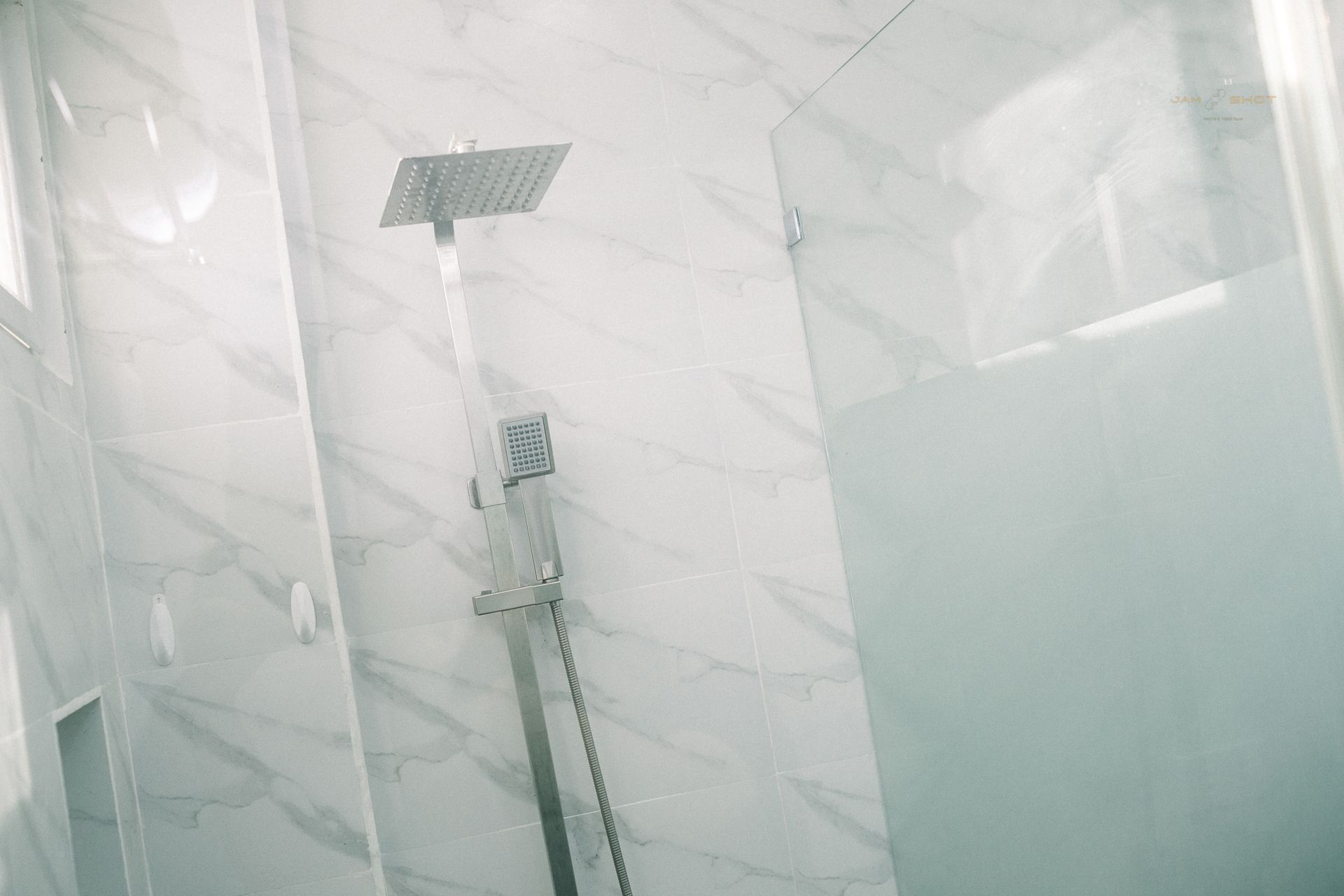 A modern shower with a square rain showerhead, chrome fixture, and white marble-patterned tile walls.