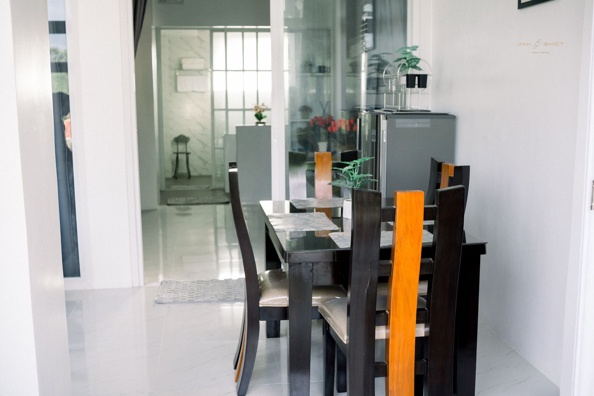 A dining area with a glass-topped table and four chairs featuring dark wood frames and central orange slats.