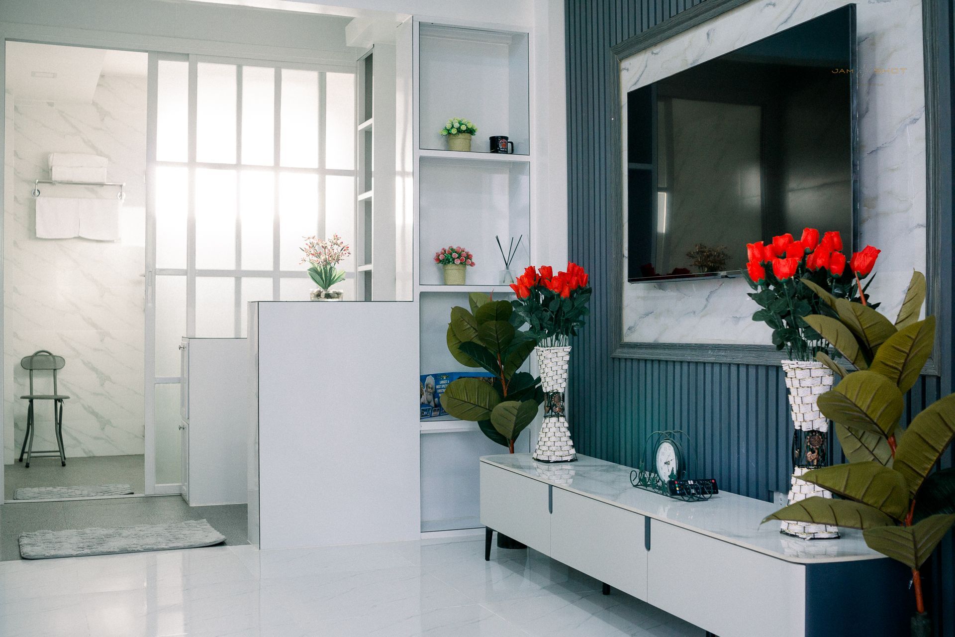 A modern living room with a wall-mounted TV, blue paneling, white storage cabinets, and bright red roses in vases.