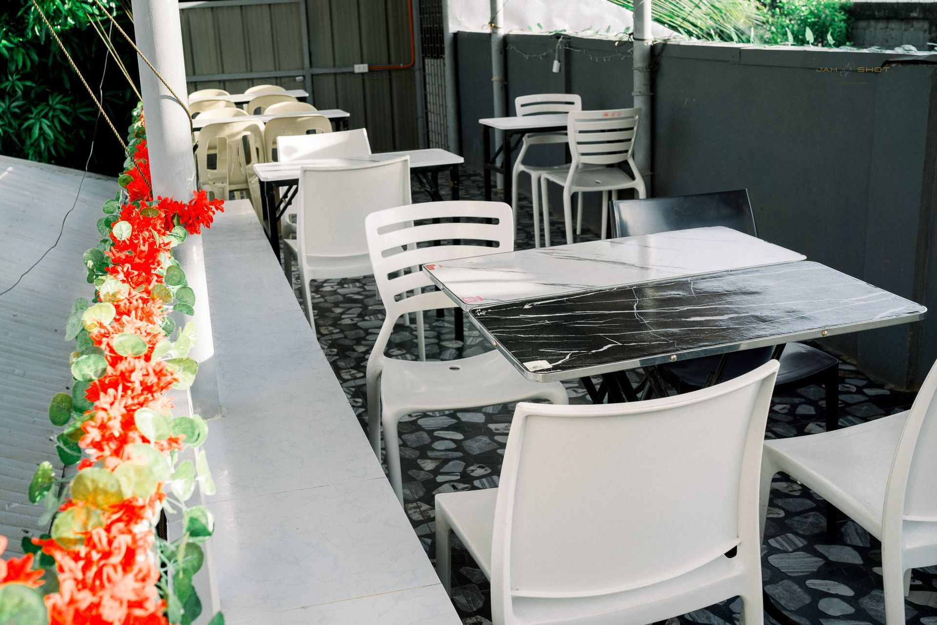 Outdoor patio with marble-topped tables, white chairs, and a decorative flower-covered railing.
